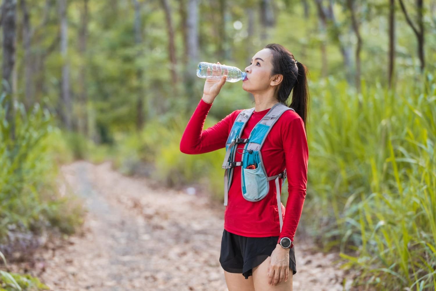 femme sportive boit de l'eau riche en potassium dans une forêt